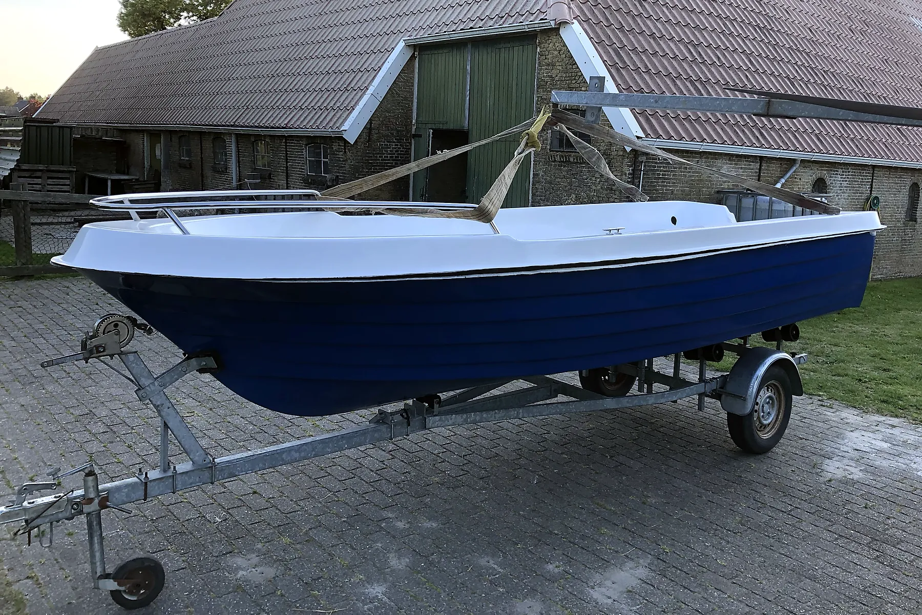 Gerestaureerde blauwe sloep op een trailer voor een Friese boerderij